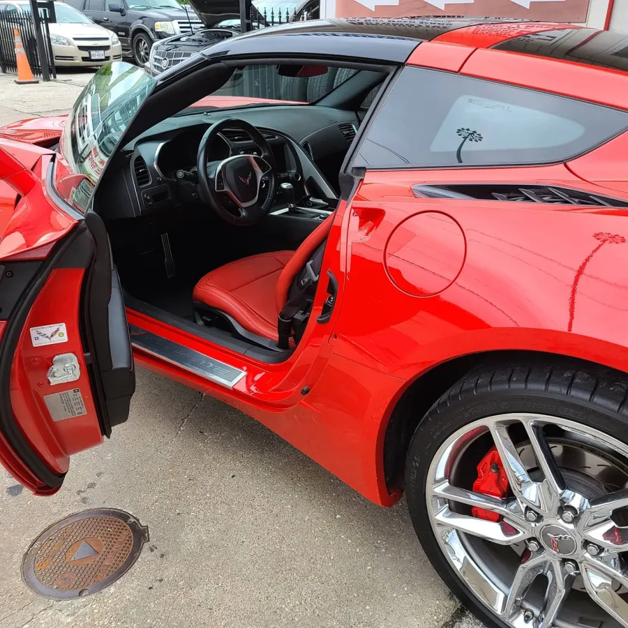 Red sports car with open door showing black and red interior, steering wheel, and shiny chrome wheels.