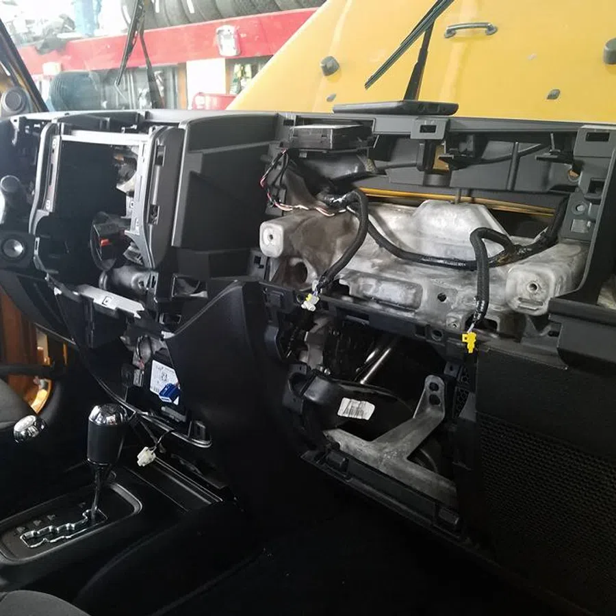 Car interior dashboard partially disassembled showing exposed wiring and components.