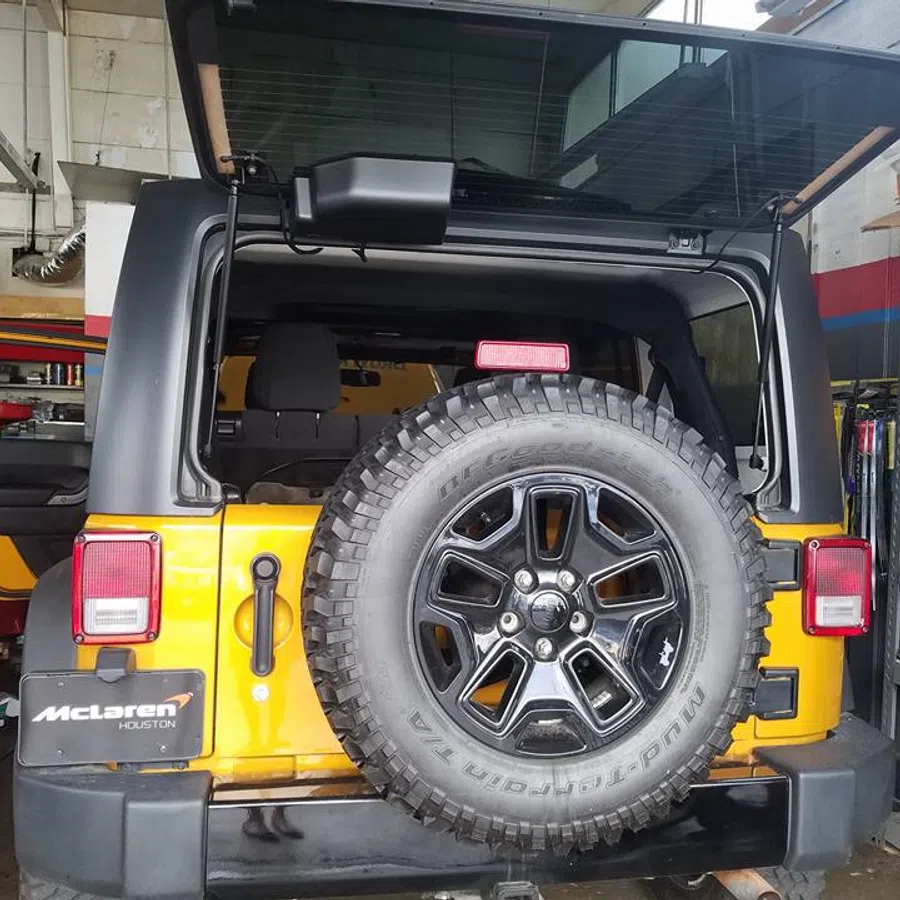 Rear view of a yellow Jeep with spare tire mounted on the back, inside an auto repair garage.