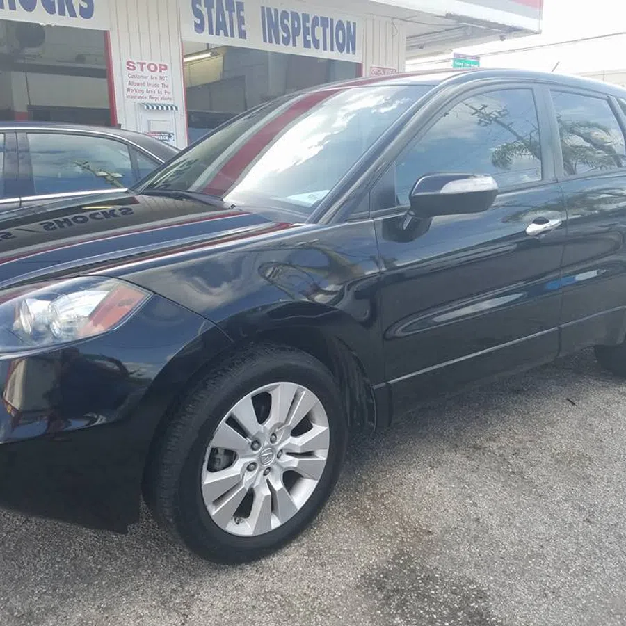 Black compact SUV parked outside a state inspection and auto service shop on a sunny day.