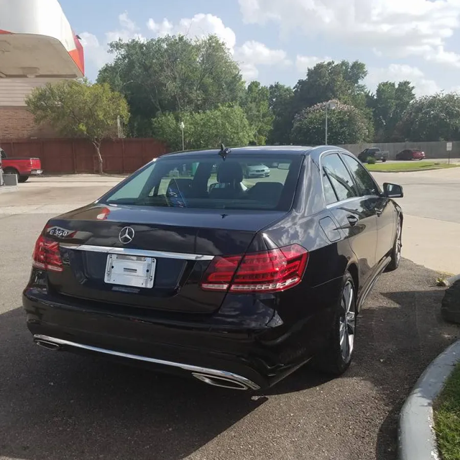 Black Mercedes-Benz E350 parked outdoors near a curb under a partly cloudy sky in a suburban area.