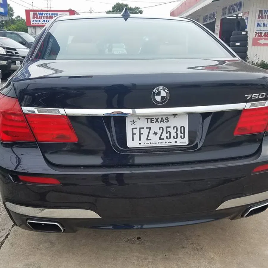 Rear view of a black BMW 750Li with Texas license plate parked outside an automotive shop.