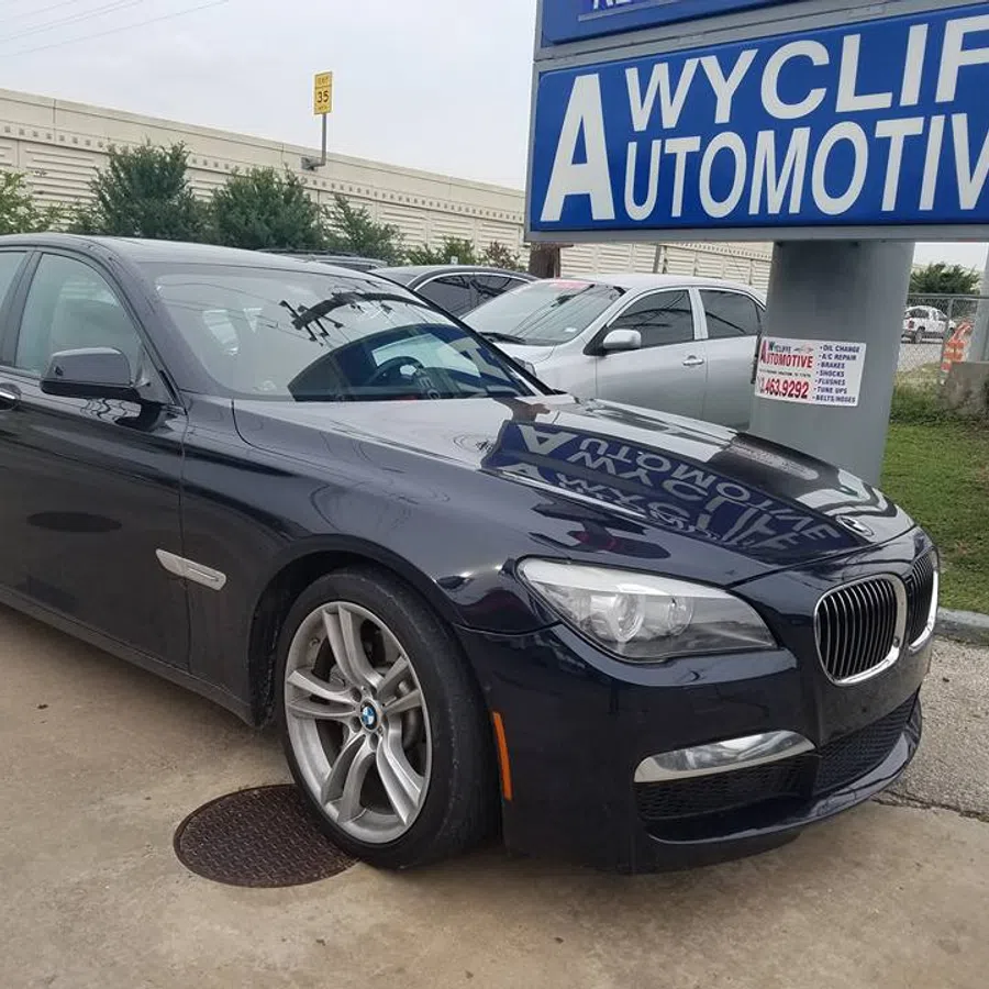 Black BMW sedan parked outside Wycliff Automotive shop under a large blue and white sign on a cloudy day.