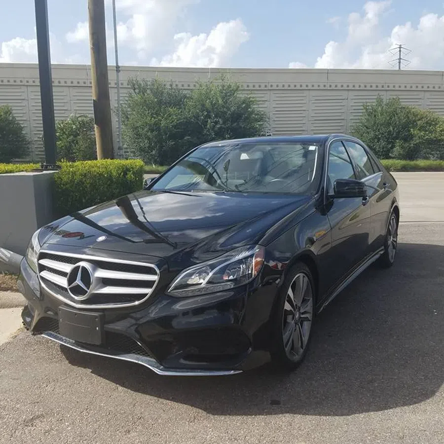 Black Mercedes-Benz sedan parked outdoors on a sunny day with greenery and a wall in the background