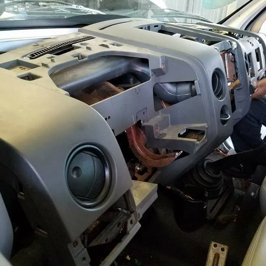 Dashboard of a vehicle removed for repair showing internal air vents and steering components with mechanic working