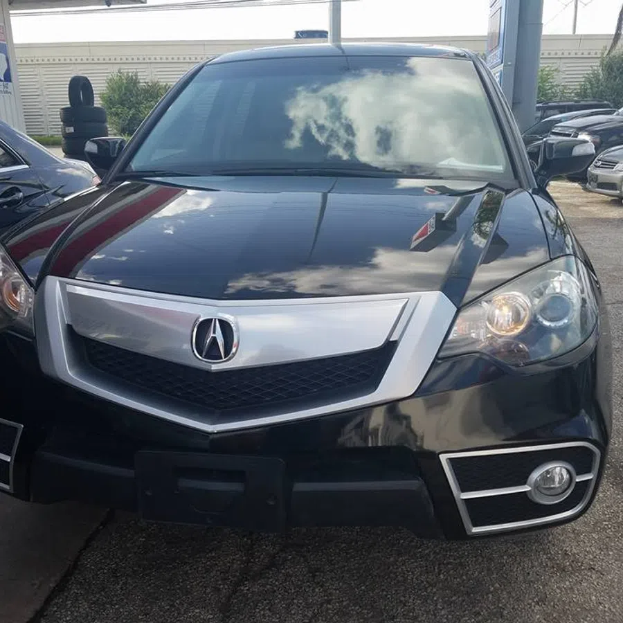 Black Acura SUV front view with chrome grille and headlights reflecting sky and surroundings.