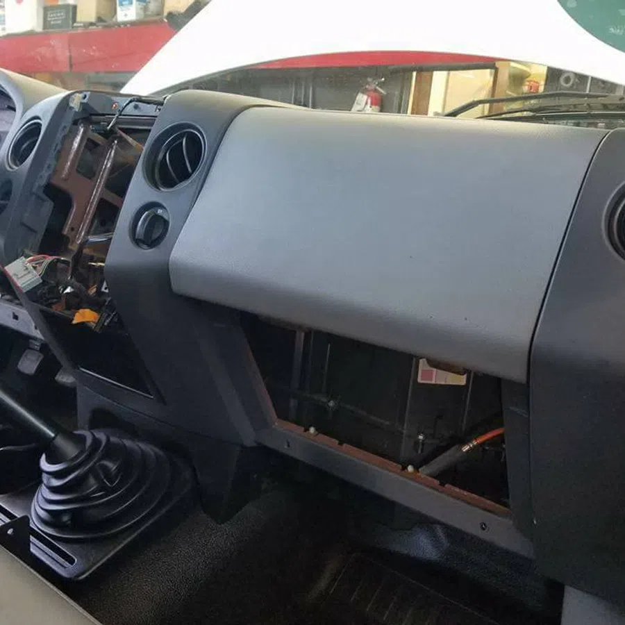 Inside view of a car dashboard with missing panels and exposed wiring near the steering wheel and glove compartment.