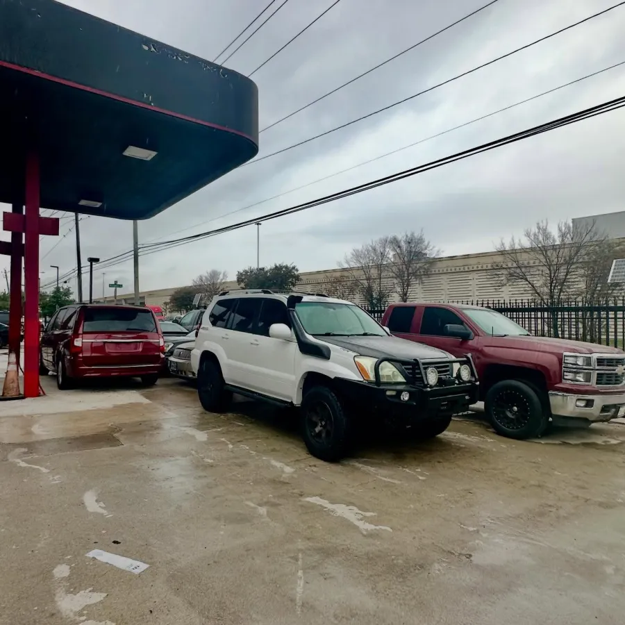 White SUV, red pickup truck, and red SUV parked outside a building under an overcast sky with power lines above.