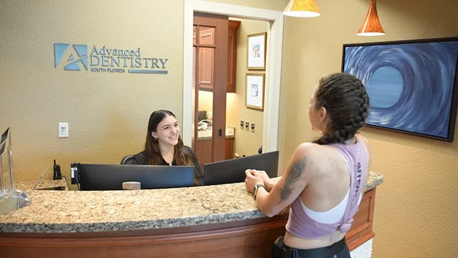 Receptionist smiling and assisting a patient at the front desk of Advanced Dentistry South Florida office.