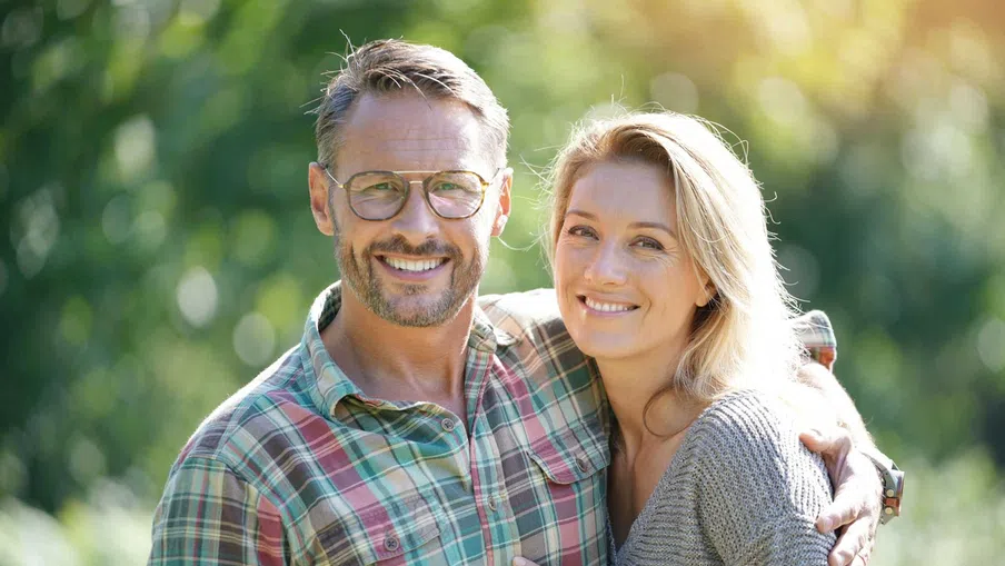 Happy young couple smiling and hugging outdoors in a sunlit park surrounded by trees and greenery.