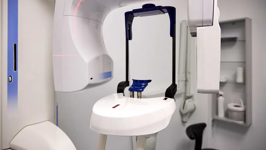 Bright modern dental clinic with dental chair, monitor, sink, and white cabinetry under natural light.