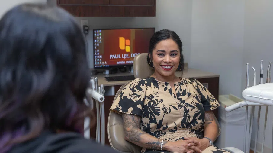 Smiling woman with tattoos sitting in dental chair during consultation in modern clinic with screen in background