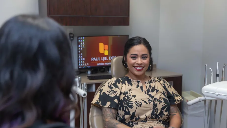 Smiling woman with tattoos sitting in dental chair during consultation in modern clinic with screen in background