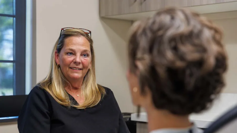 Female healthcare professional in black scrubs talking with a patient in a medical office setting.
