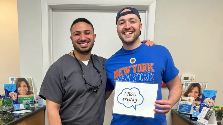 Smiling dental patient and dentist standing together holding a flossing sign at dental office reception.