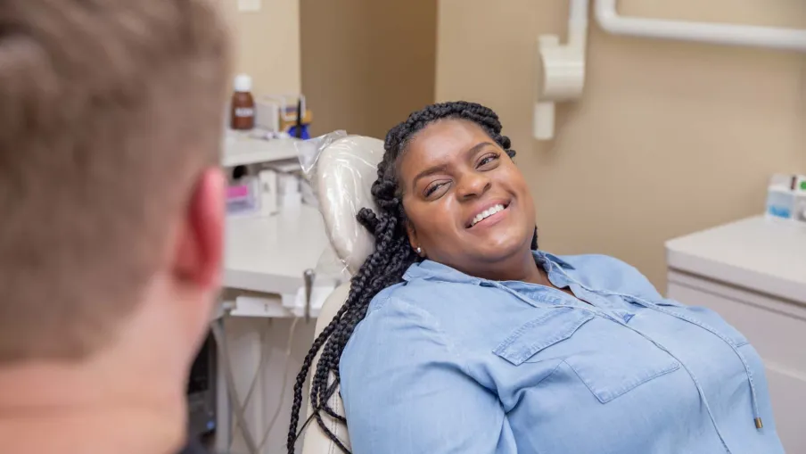 Smiling woman in a dental chair speaking with a male dentist during a checkup in a clinic room.