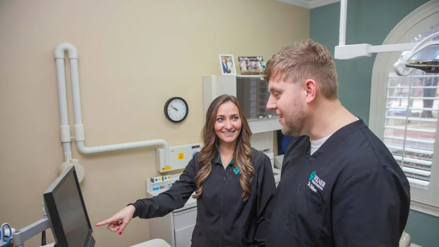 Two dental professionals discussing digital records on a computer in a bright clinic room.