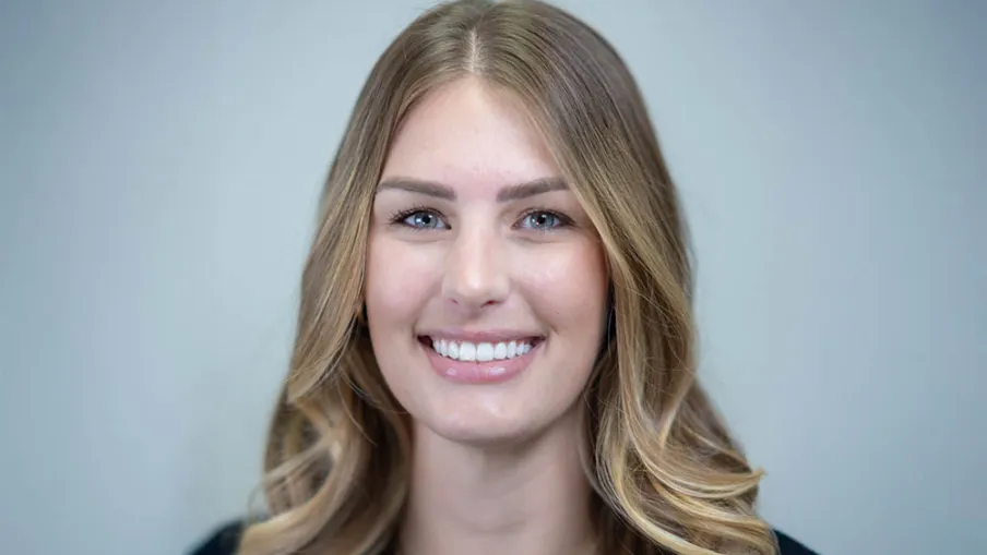 Smiling young woman with wavy blonde hair and blue eyes wearing a black top and layered necklaces.