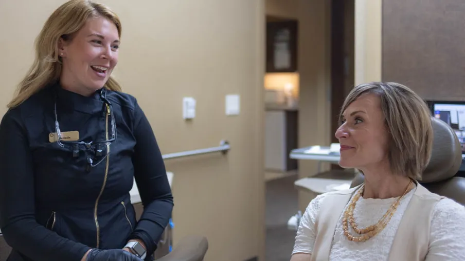 Dentist and patient smiling and conversing in a dental office during a consultation.