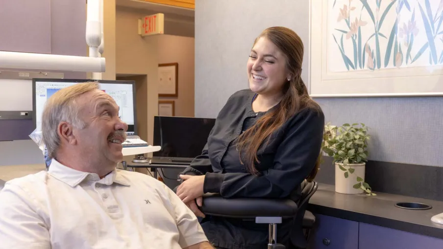 Smiling dental hygienist talking with male patient in modern dental office setting