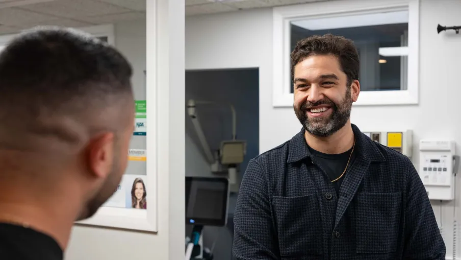 Two men smiling and talking in a modern indoor office setting with computer equipment in the background