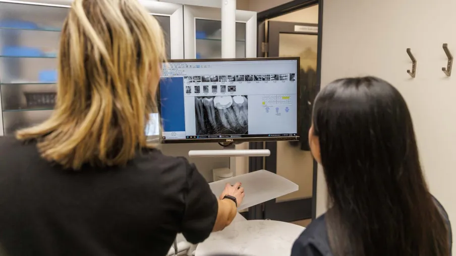 Dentist reviewing dental x-rays on a computer screen with a patient in a dental office setting.