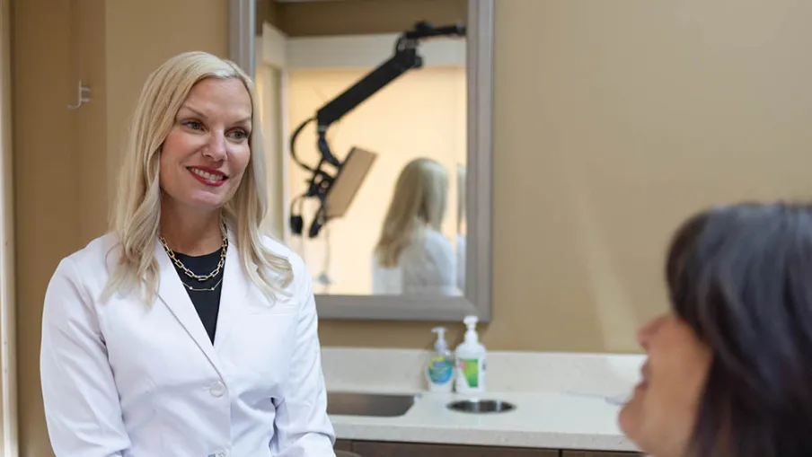Female doctor in white coat smiling and talking to a female patient in a medical office.