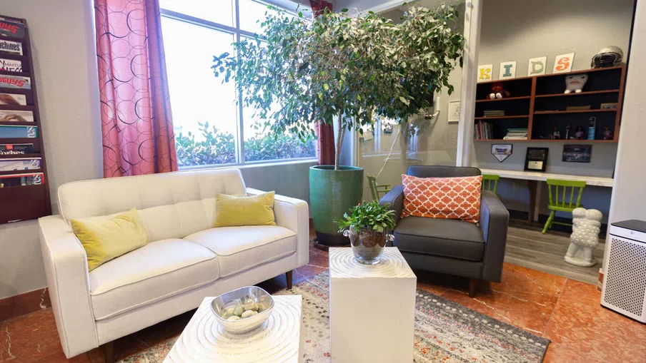 Modern living room with white sofa, gray armchair, green plants, and bright natural light from large window.