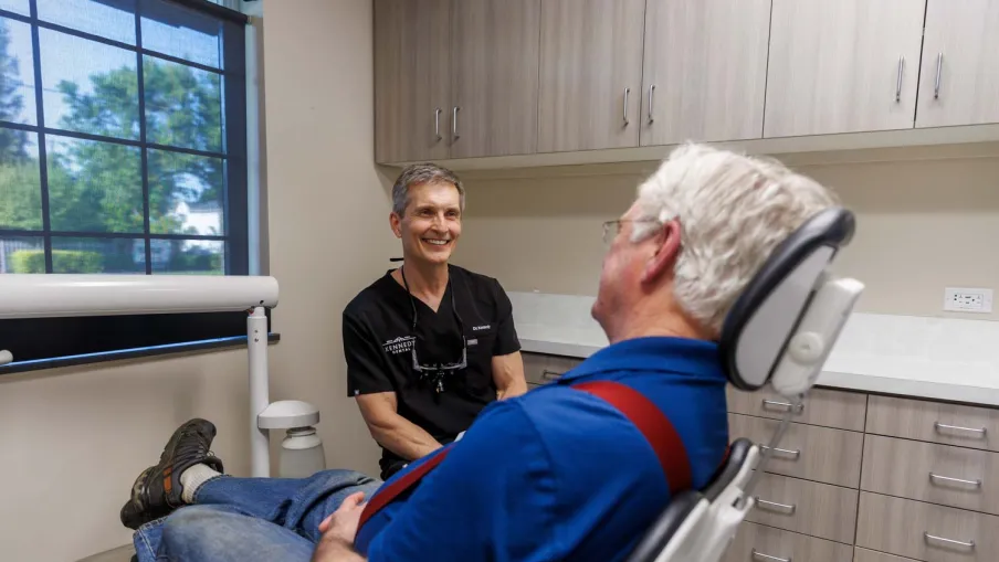 Bright modern dental clinic with dental chair, monitor, sink, and white cabinetry under natural light.