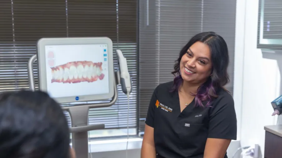Dentist consulting with patient using dental imaging technology showing teeth alignment on screen.