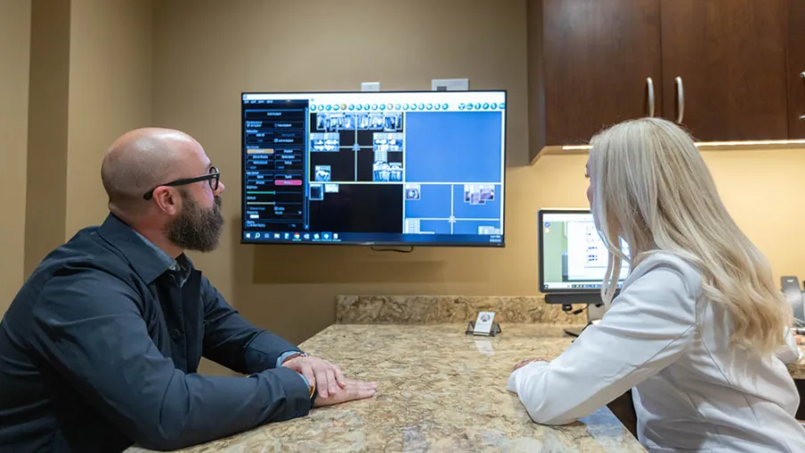 Man and woman discussing surveillance footage displayed on a wall-mounted monitor in an office setting.