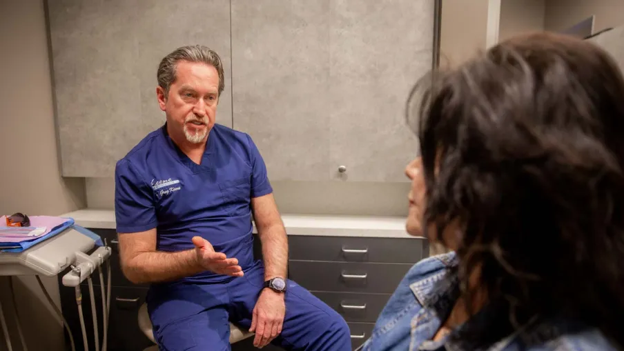 Dentist in blue scrubs consulting with a patient in a modern dental office setting.