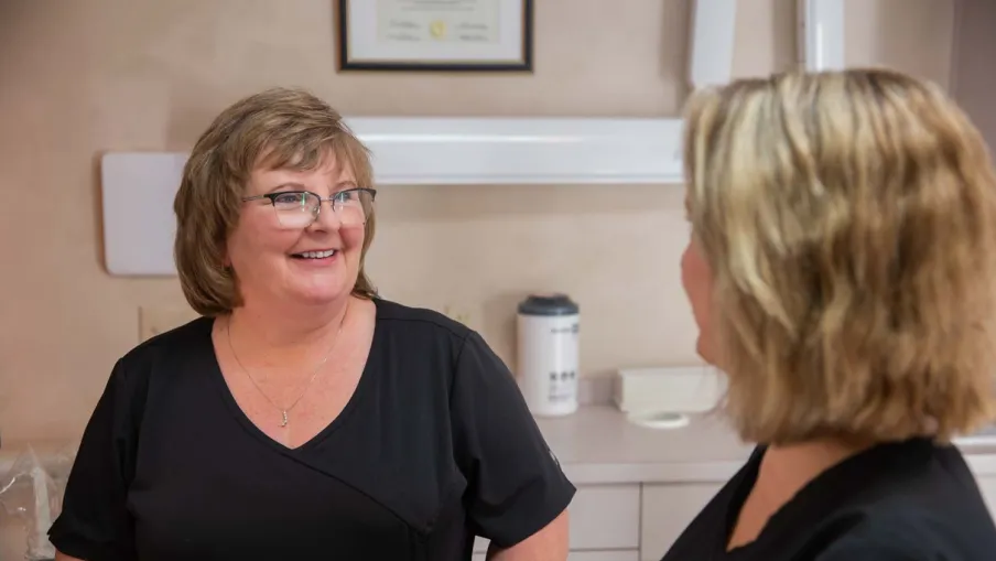 Two smiling women in black scrubs having a friendly conversation in a medical office setting
