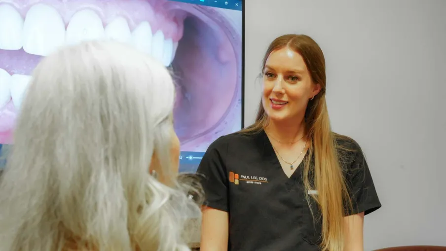 Female dentist consulting an elderly patient with dental x-ray images displayed on a screen in the background
