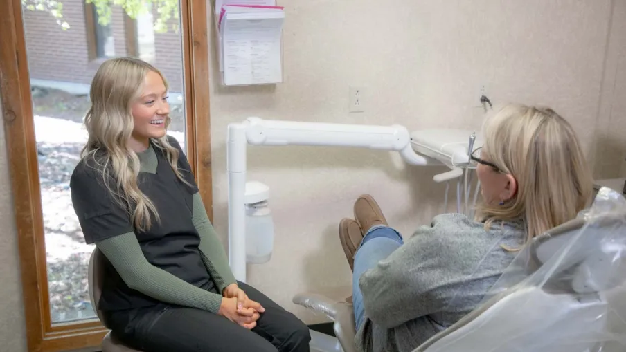 Female dentist consulting with female patient sitting in a dental chair in bright clinic.