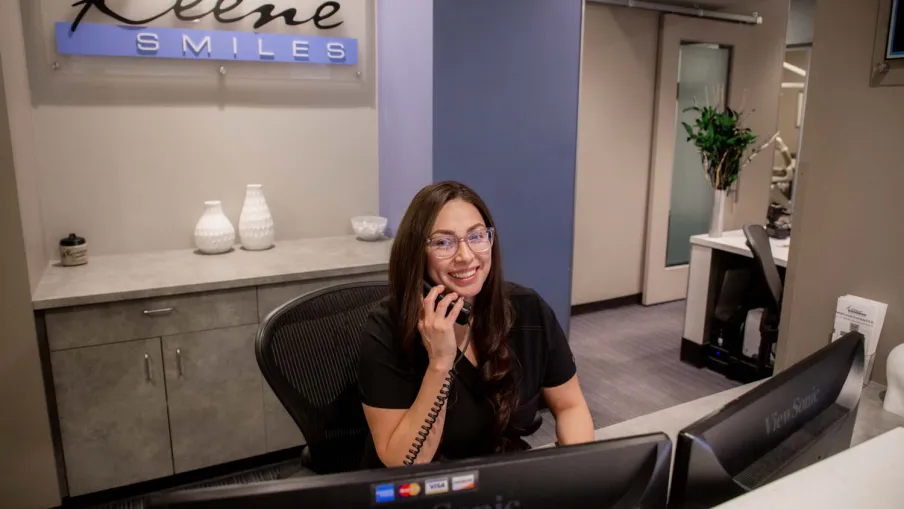 Receptionist smiling while talking on phone at Keene Smiles dental office front desk