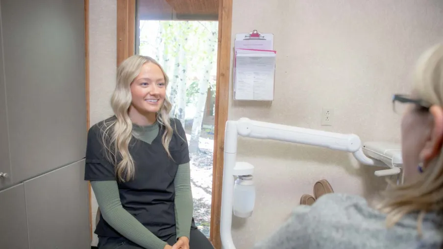 Smiling female healthcare worker wearing scrubs sitting and talking to a patient in a bright clinic room