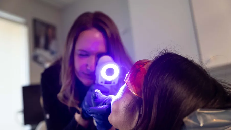 Dermatologist using a handheld device emitting blue light to examine a patient's skin in a clinical setting