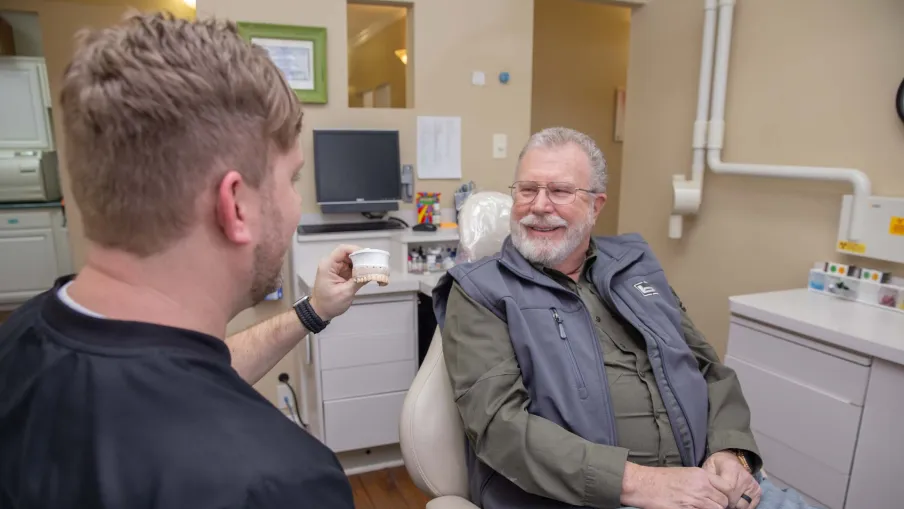 Dentist showing a dental mold to a senior male patient in a dental office during consultation.