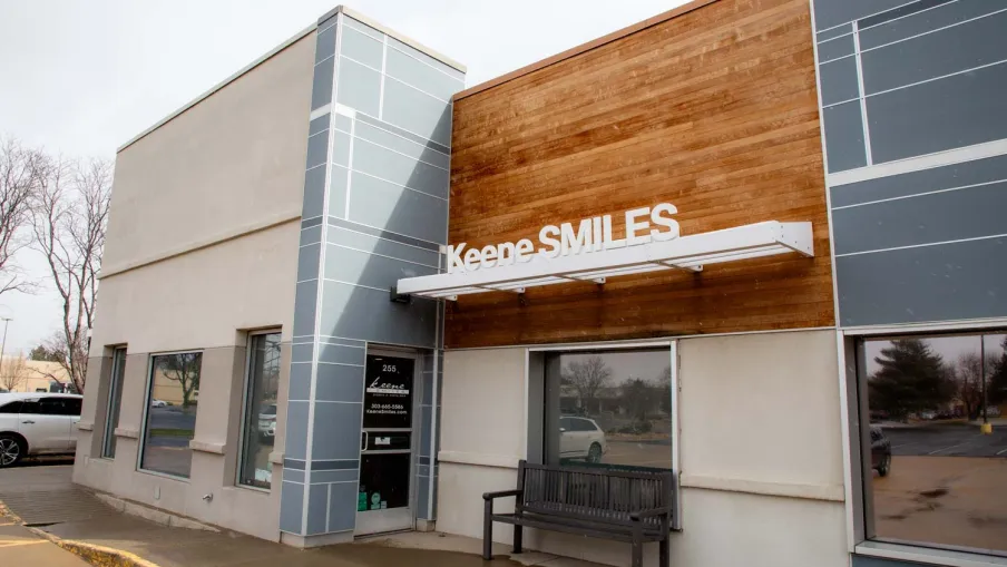 Modern dental office exterior with wood paneling, large windows, and a bench outside Keene SMILES clinic.