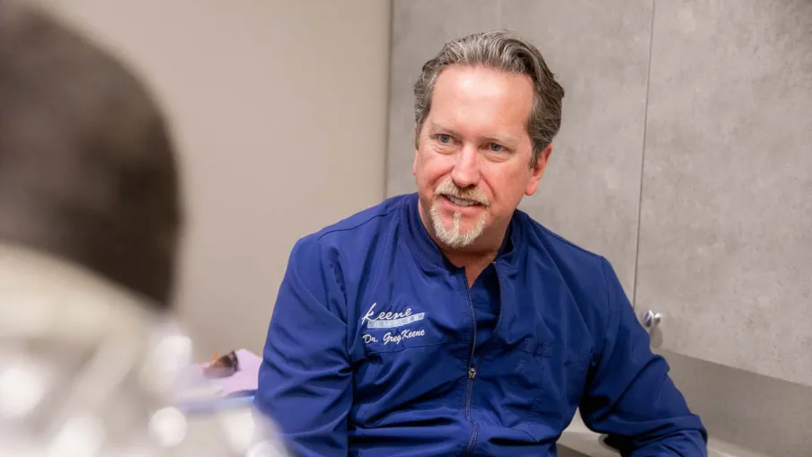 Male dentist in blue coat consulting a patient in a dental office, smiling and engaging in discussion