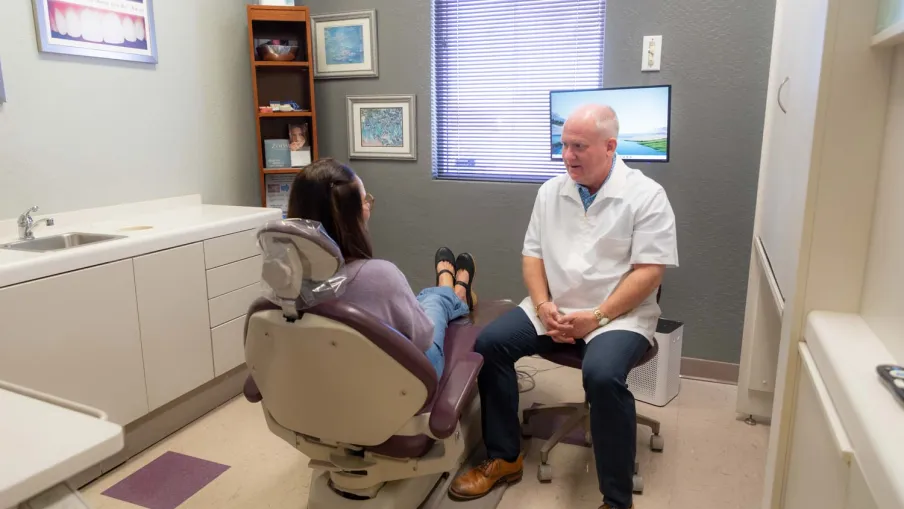 Dentist consulting female patient seated in dental chair inside a modern clinic room with medical equipment