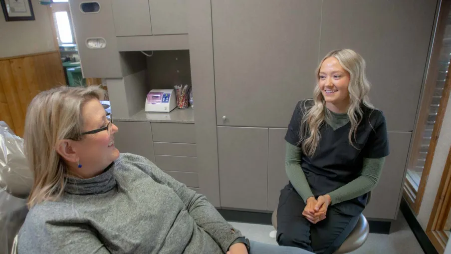 Dental hygienist smiling and talking with a patient in a modern dental clinic room.