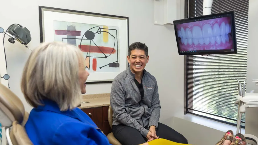 Dentist and patient smiling in a consultation room with dental X-ray on screen and modern decor.