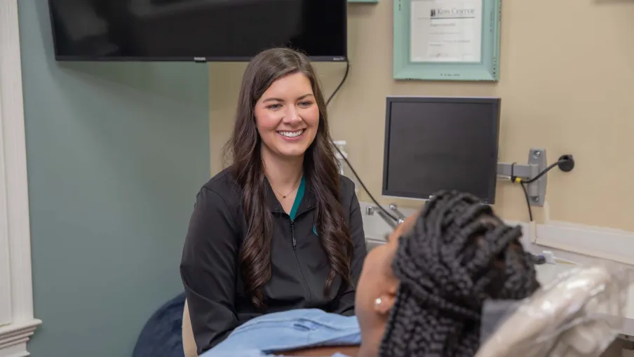 Smiling dental professional talking to patient reclining in dental chair in a modern clinic.