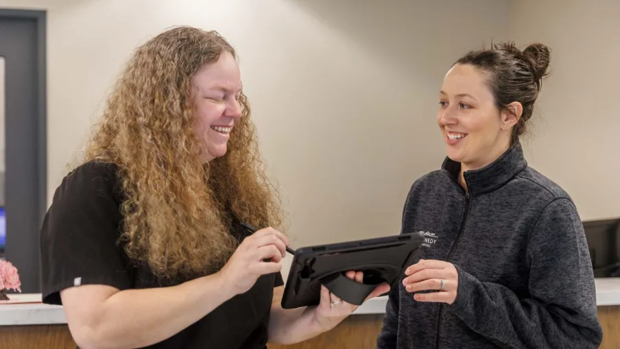 Two women smiling and discussing while using a tablet in a professional indoor setting