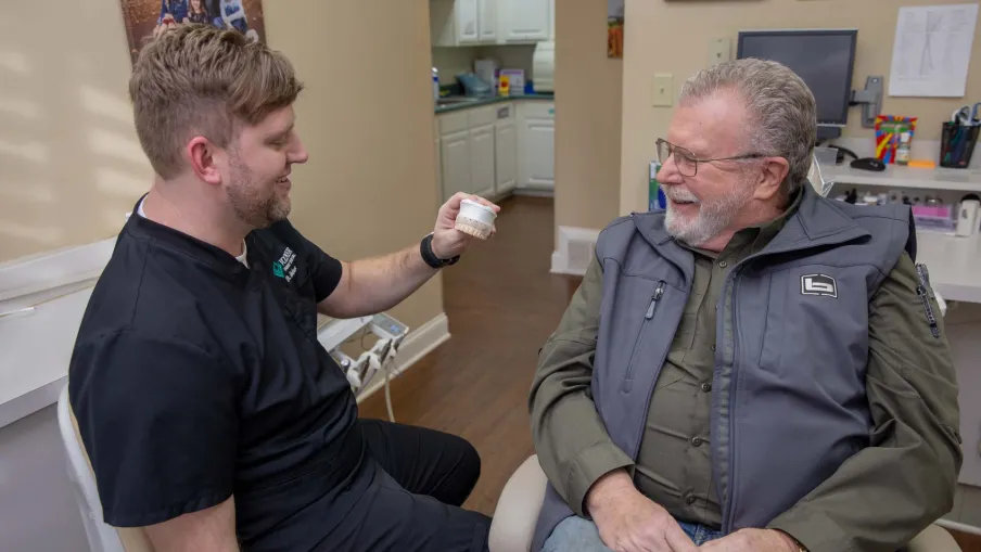 Dentist showing dental impression mold to smiling senior male patient in dental office