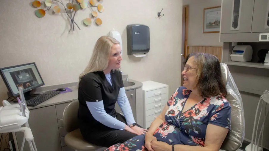 Dentist attentively consulting with female patient in floral dress in dental clinic room.