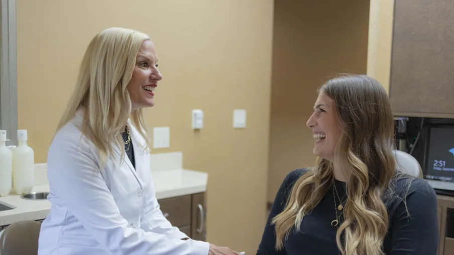 Doctor in white coat smiling and talking with a female patient in a medical office setting