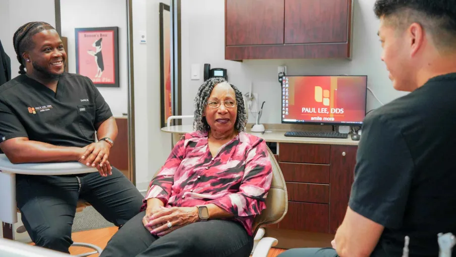Dentist and dental assistant talk with a female patient in a modern dental office during consultation.